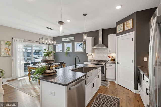 kitchen with white cabinetry, stainless steel appliances, a kitchen island with sink, and wall chimney range hood