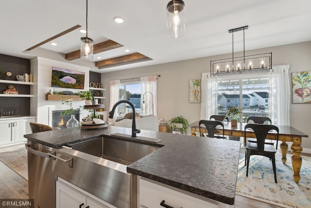 kitchen featuring a fireplace, an island with sink, wood-type flooring, sink, and white cabinets