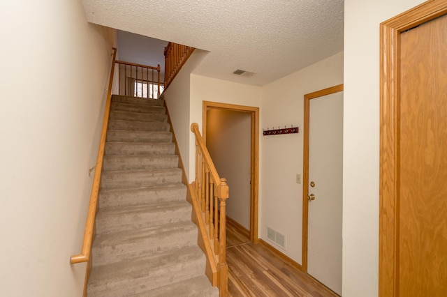 stairway featuring visible vents, a textured ceiling, and wood finished floors