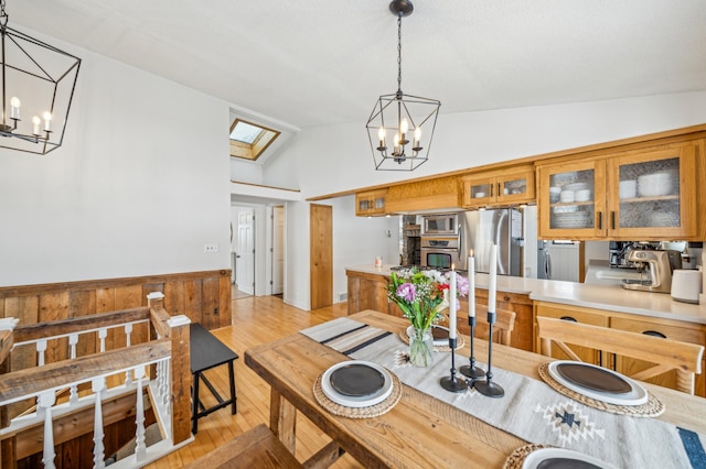 dining area featuring vaulted ceiling with skylight, an inviting chandelier, and light hardwood / wood-style flooring