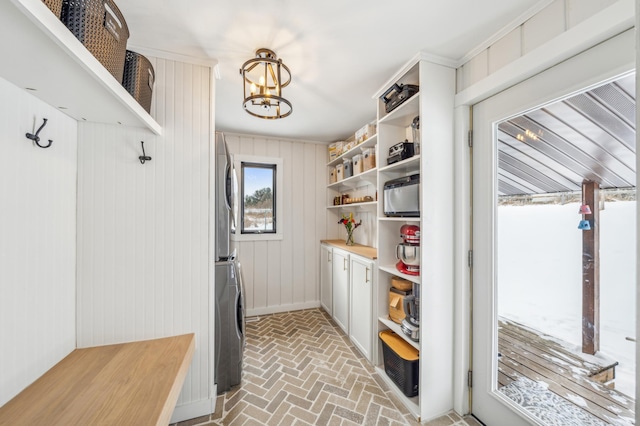 mudroom with baseboards, stacked washer / drying machine, brick floor, and an inviting chandelier