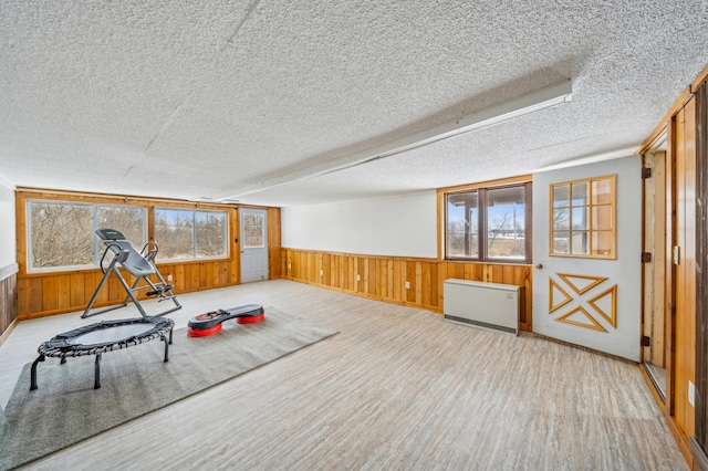 workout area featuring wood walls, light hardwood / wood-style flooring, a textured ceiling, and a wealth of natural light