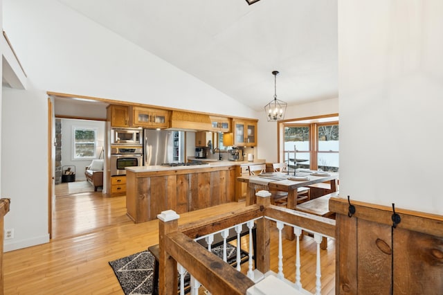 kitchen with a chandelier, hanging light fixtures, kitchen peninsula, stainless steel appliances, and light hardwood / wood-style flooring