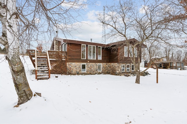 snow covered back of property with stone siding, a deck, and stairs