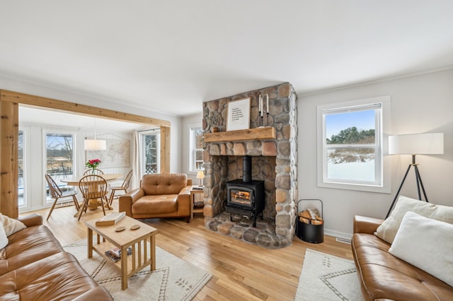 living room with a wood stove, light wood finished floors, baseboards, and ornamental molding