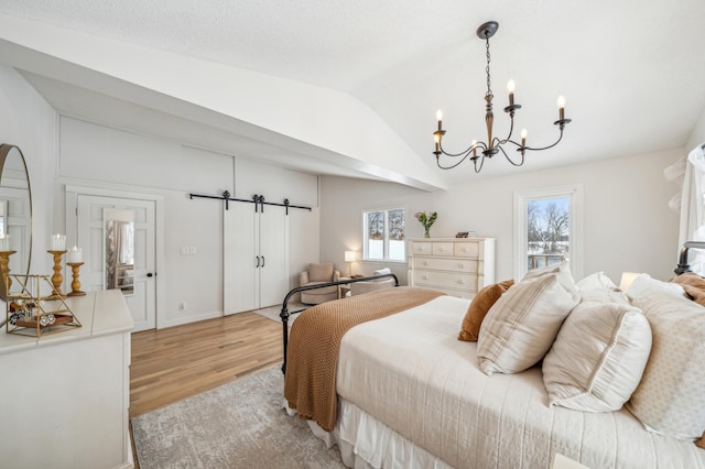 bedroom with vaulted ceiling, a barn door, and light wood finished floors