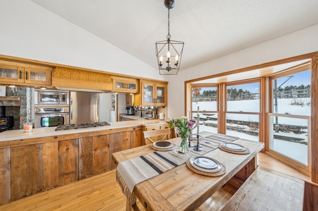 dining area with lofted ceiling, light wood-style flooring, a chandelier, and a wood stove