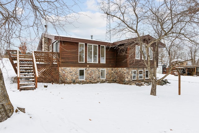 snow covered back of property featuring stone siding, stairway, and a wooden deck