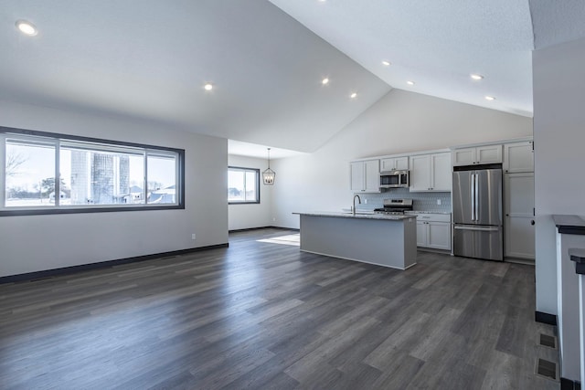 kitchen with appliances with stainless steel finishes, white cabinets, decorative backsplash, dark wood-type flooring, and a center island with sink