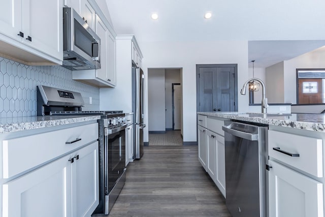 kitchen with appliances with stainless steel finishes, pendant lighting, white cabinetry, backsplash, and light stone countertops