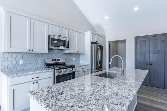 kitchen featuring sink, vaulted ceiling, appliances with stainless steel finishes, an island with sink, and light stone countertops