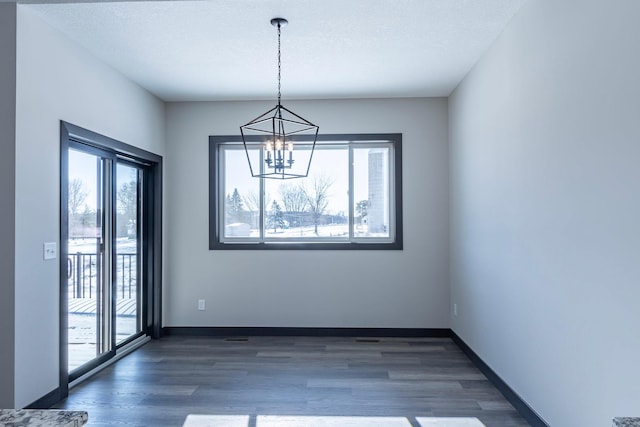 unfurnished dining area with dark wood-type flooring, a healthy amount of sunlight, a chandelier, and a textured ceiling