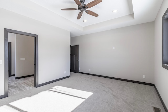 unfurnished bedroom featuring light colored carpet, a raised ceiling, and ceiling fan