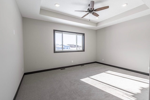 carpeted empty room with ceiling fan and a tray ceiling