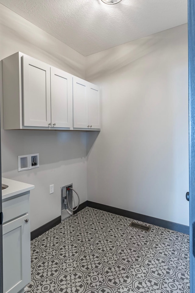 clothes washing area featuring cabinets, light tile patterned flooring, hookup for a washing machine, and a textured ceiling