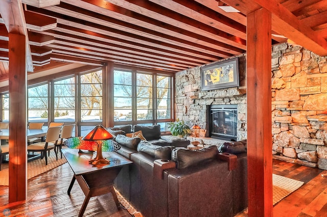 living area with a stone fireplace, beamed ceiling, and wood finished floors