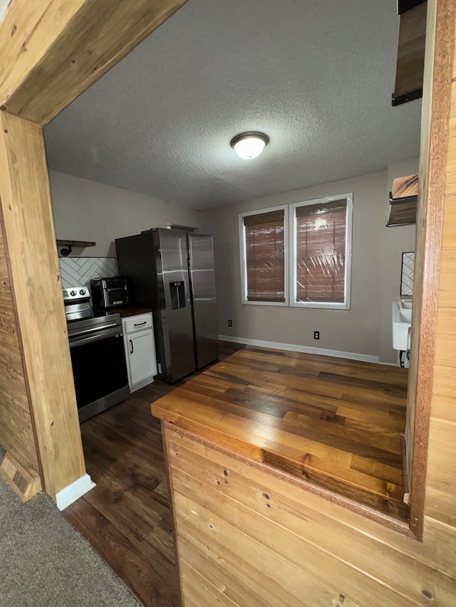 kitchen featuring wood counters, white cabinetry, a textured ceiling, appliances with stainless steel finishes, and dark hardwood / wood-style floors