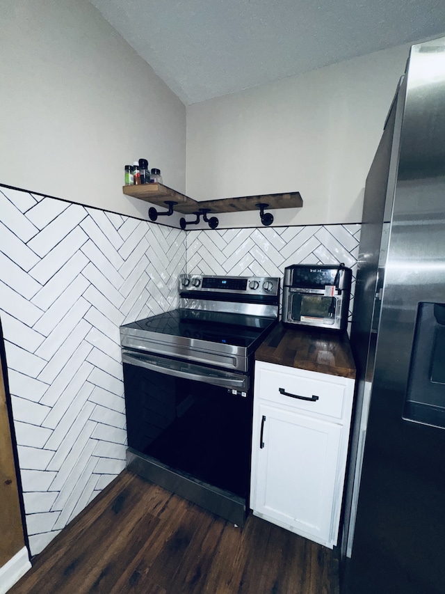 kitchen with white cabinetry, vaulted ceiling, tile walls, appliances with stainless steel finishes, and dark hardwood / wood-style floors