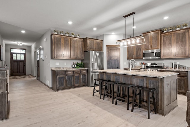 kitchen with stainless steel appliances, an island with sink, hanging light fixtures, and dark brown cabinets