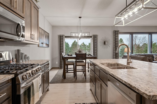 kitchen with appliances with stainless steel finishes, decorative light fixtures, an island with sink, sink, and light hardwood / wood-style floors