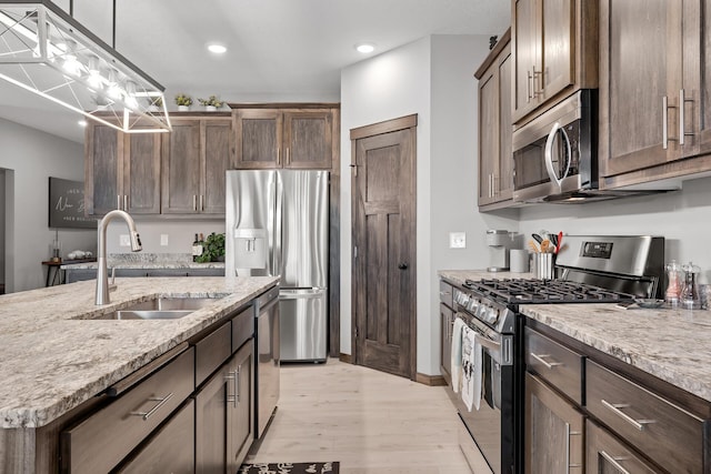 kitchen featuring pendant lighting, sink, stainless steel appliances, light stone counters, and light wood-type flooring