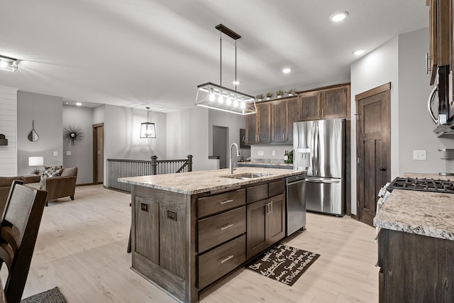 kitchen featuring appliances with stainless steel finishes, sink, hanging light fixtures, light stone countertops, and a center island with sink