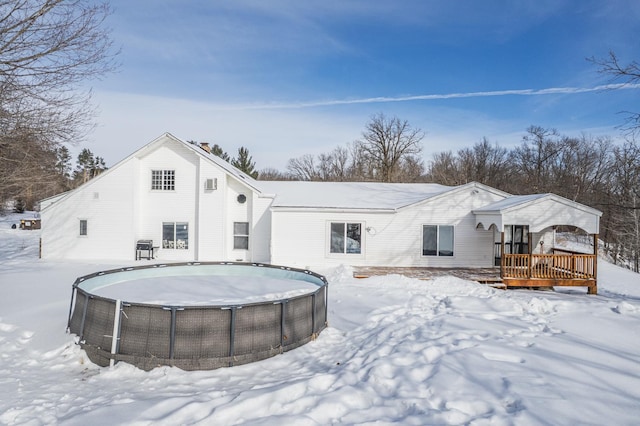 snow covered rear of property featuring a deck and an outdoor pool