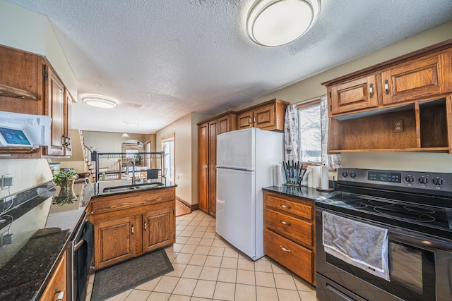 kitchen with light tile patterned floors, electric range, brown cabinets, freestanding refrigerator, and a sink