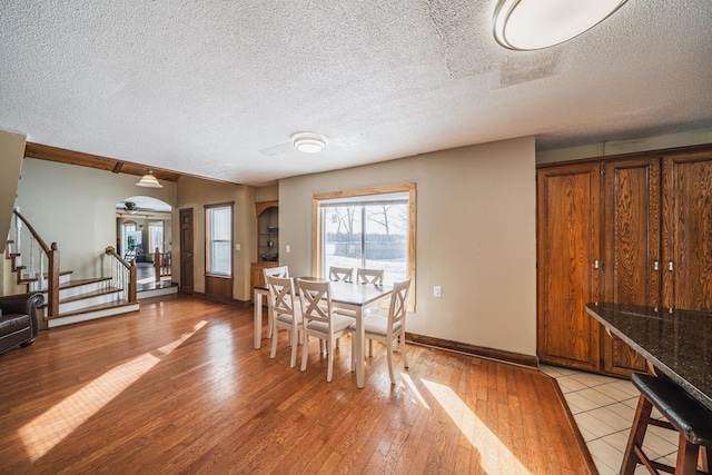 dining space featuring a textured ceiling, stairway, light wood-style flooring, and baseboards