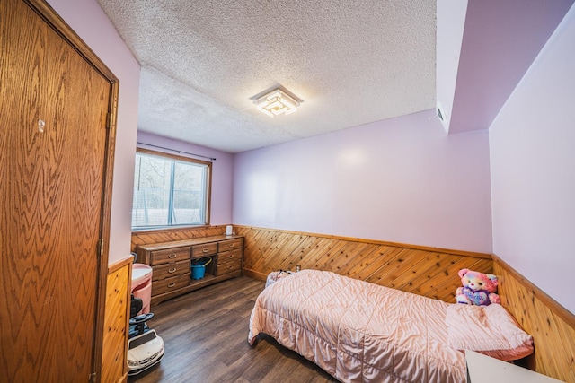 bedroom featuring wainscoting, wooden walls, a textured ceiling, and wood finished floors