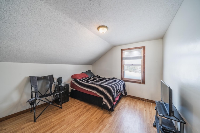 bedroom featuring vaulted ceiling, a textured ceiling, baseboards, and wood finished floors