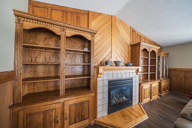 living area with lofted ceiling, a textured ceiling, dark wood-type flooring, wood walls, and a fireplace