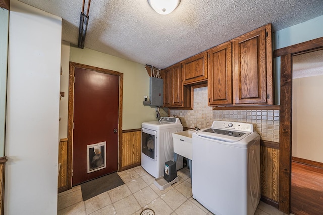 washroom with a textured ceiling, washing machine and dryer, wainscoting, cabinet space, and electric panel