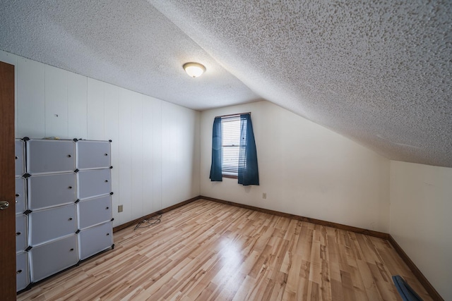 bonus room with a textured ceiling, vaulted ceiling, wood finished floors, and baseboards