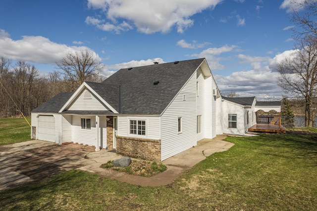 back of property with a garage, aphalt driveway, roof with shingles, brick siding, and a yard