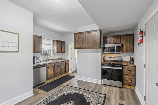 kitchen featuring sink, dark stone countertops, light hardwood / wood-style floors, stainless steel appliances, and a textured ceiling