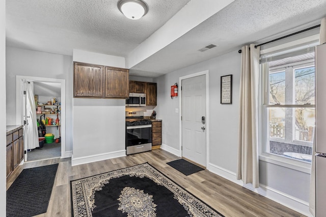 kitchen with appliances with stainless steel finishes, a textured ceiling, and light hardwood / wood-style floors