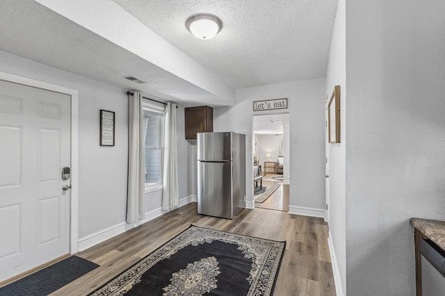 kitchen with dark wood-type flooring, stainless steel fridge, and a textured ceiling