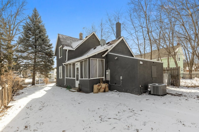 snow covered back of property featuring central AC and a sunroom