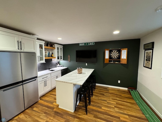 kitchen with dark wood-type flooring, stainless steel fridge, white cabinetry, a kitchen island, and a kitchen bar