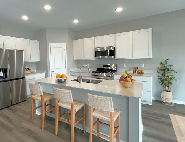 kitchen with a kitchen island with sink, white cabinetry, stainless steel appliances, and a kitchen breakfast bar