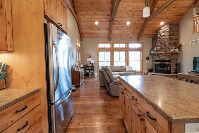 kitchen with wood ceiling, stainless steel refrigerator, lofted ceiling with beams, dark hardwood / wood-style flooring, and a stone fireplace