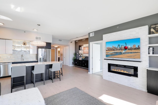 living room with visible vents, light wood-style floors, and a glass covered fireplace