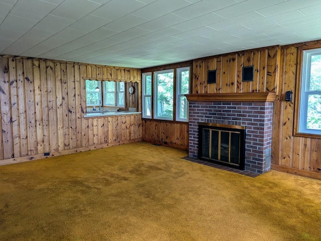 unfurnished living room featuring a brick fireplace, a wealth of natural light, wooden walls, and carpet flooring