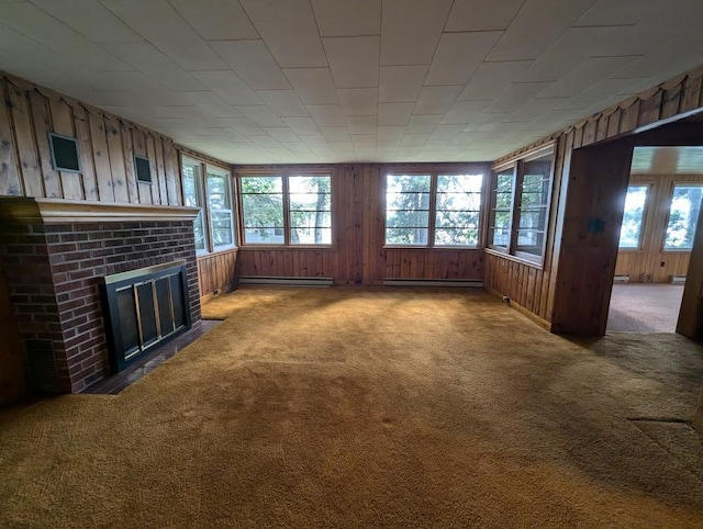 unfurnished living room with a brick fireplace, a baseboard radiator, wood walls, and carpet