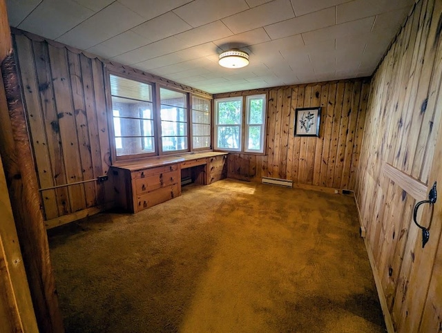 unfurnished office with dark colored carpet, wood walls, built in desk, and a baseboard heating unit