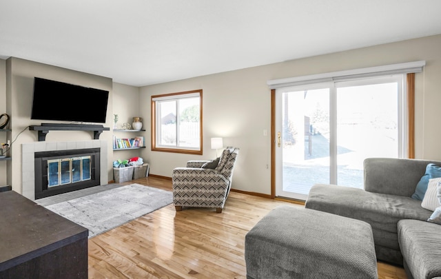 living room featuring a tile fireplace, a healthy amount of sunlight, and hardwood / wood-style floors