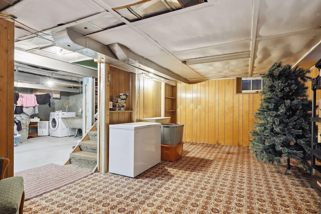 basement featuring washing machine and clothes dryer, refrigerator, and wood walls