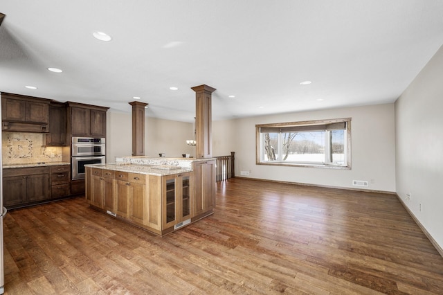 kitchen featuring visible vents, baseboards, wood finished floors, ornate columns, and double oven