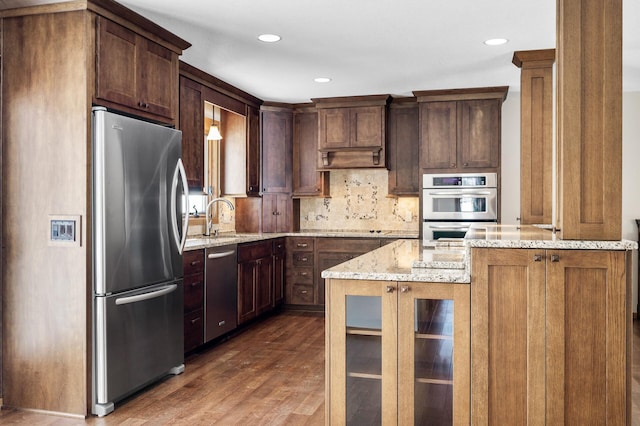 kitchen with light stone counters, stainless steel appliances, backsplash, a sink, and wood finished floors